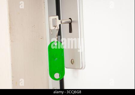 Key with green keychain inserted in doorlock close-up Stock Photo