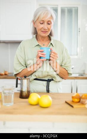 Cheerful senior woman having breakfast with cup of coffee Stock Photo