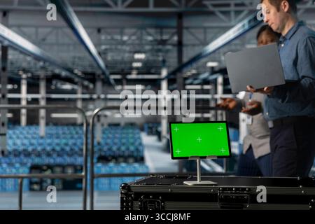 Server room colleagues managing large scale IT infrastructure using mockup device. Close up of green screen tablet in front of data center admins coordinating deployment of new server architectures Stock Photo