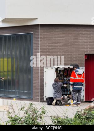 Paris, France - Nov 8, 2023: Two technicians working on an open street control cabinet in an urban area, handling electric wires and components near a Stock Photo