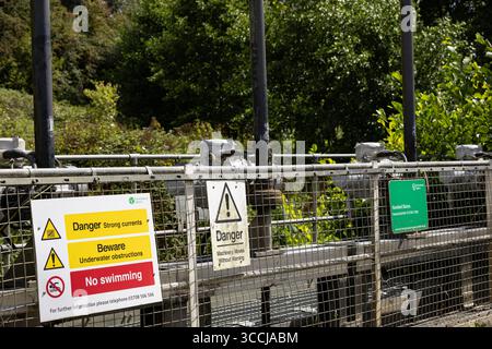 Warning signs on a metal fence near a river weir, cautioning about strong currents, underwater obstructions, and no swimming Hazeland Ratford Calne Stock Photo