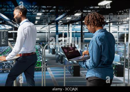 Woman expert in data center stressed by critical error popup on laptop during diagnostics session on industrial platform. Anxious staff troubleshooting system fault affecting performance. Stock Photo