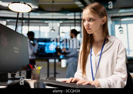 Anxious junior dev debugging code in office, looking for solutions to fix errors on PC display. Concerned system administrator reviewing error logs at computer, trying to to resolve critical glitches Stock Photo