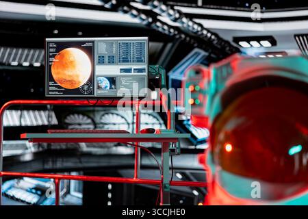 Red ambient light in spacecraft over Mars analysis displayed on screen. Futuristic spaceship cockpit control terminals showing planetary data during crewed mission to red planet Stock Photo