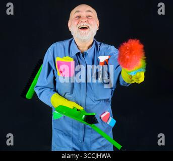 Big cleaning. Smiling man in uniform with dust brush, broom and dustpan. Professional cleaning service. Cleaner in rubber gloves with sweeping tools Stock Photo