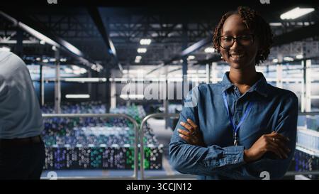 Portrait of smiling data center admin next to coworkers running diagnostics on equipment to identify errors. Happy woman next to IT experts working to prevent failure and minimize downtime, Stock Photo