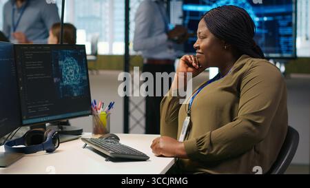 Jolly female programmer at office desk pleased after developing application using machine learning automation. Joyous employee satisfied after debugging applications using neural networks, camera A Stock Photo