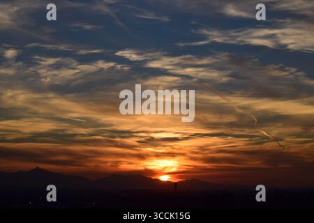 A dramatic horizon sunset casting intense gold and deep orange light across a layered sky filled with sweeping cirrus clouds Stock Photo