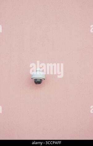 Security camera mounted on a pink wall in bright daylight Stock Photo