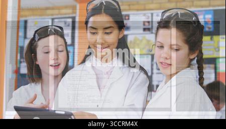 Students wearing lab coats and goggles examining tablet in science lab, with posters and boards Stock Photo