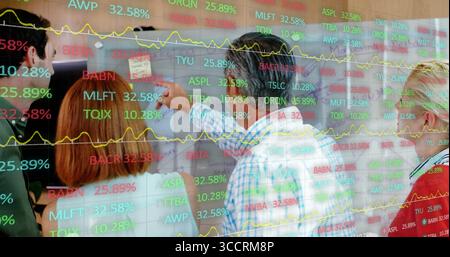 Group of financial analysts discussing data in room, with whiteboard charts and tickers Stock Photo