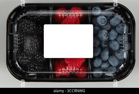 Fresh blackberries, blueberries, and raspberries in a clear plastic box with a blank white label isolated nature background with clipping path Stock Photo