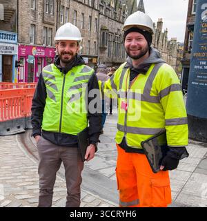 Two male construction workers wearing high visibility vest, jacket and hardhats standing at job site, High Street, Edinburgh, Scotland, United Kingdom Stock Photo