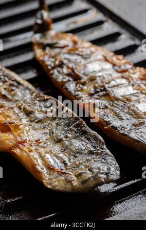 Smoked mackerel fillets cooking on a cast iron skillet griddle background backdrop. Stock Photo