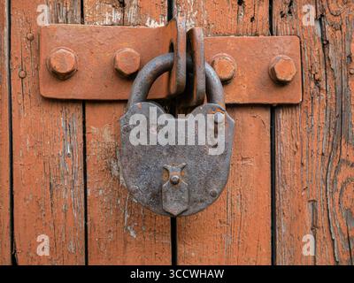 Old rusty padlock locks light brown wooden gate with peeling paint close-up. Stock Photo