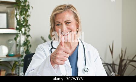 Smiling Senior Doctor Giving Thumbs Up in Her Medical Office Stock Photo