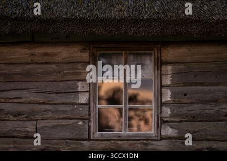 Rustic Log cabin and window with a reflection of sunrise. Old wooden log house window background. Stock Photo