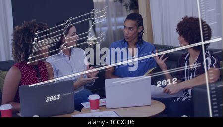 Collaborating coworkers around table in office lounge, with laptops, coffee cups, timeline graphics Stock Photo