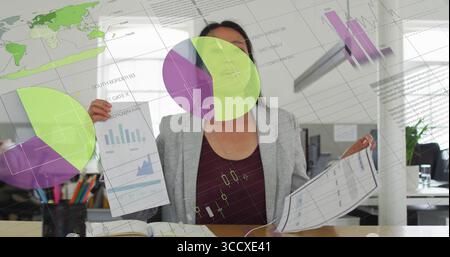 Businesswoman wearing business attire analyzing printed data reports in office, with digital charts Stock Photo