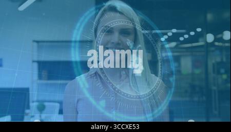 Smiling business woman pointing at holographic interface in office, with circular HUD elements Stock Photo