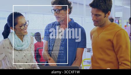 Reviewing laptop screen by three professionals in open-plan office, with digital code overlay Stock Photo