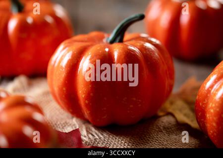 Small orange pumpkins on a rustic wooden table with scattered autumn leaves in warm red, yellow, and brown tones. Stock Photo