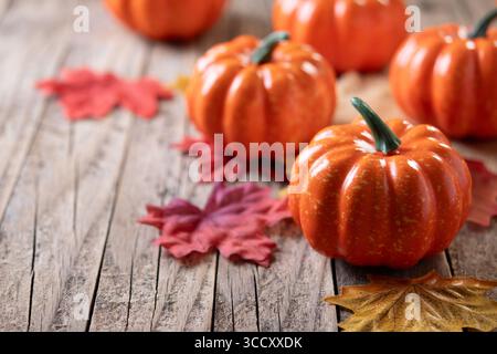 Small orange pumpkins on a rustic wooden table with scattered autumn leaves in warm red, yellow, and brown tones. Stock Photo