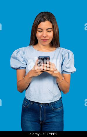 Young woman using smartphone on blue background: concentrated female browsing internet on mobile phone Stock Photo