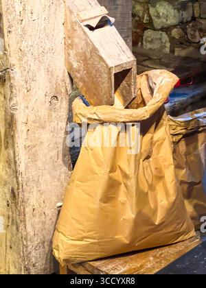 Fresh flour being poured from a wooden chute a paper sack at an old town mill in a rustic setting Stock Photo