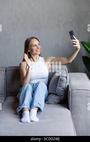 Happy beautiful young blogger woman waving greeting hand at camera, saying hello to audience, talking on video conference call, broadcasting on Intern Stock Photo