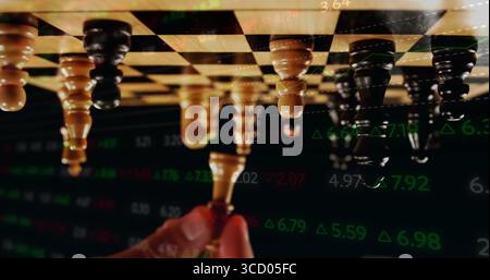 Grasping light pawn by adult hand making move on wooden chessboard, with stock market overlay Stock Photo