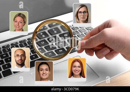 Recruiter with magnifying glass and candidates' photos at table, closeup. Human resources management Stock Photo