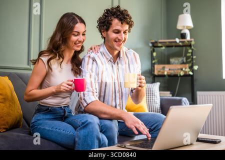 Adult couple is having video call with family. Man and woman sitting at sofa at home and using laptop. Stock Photo