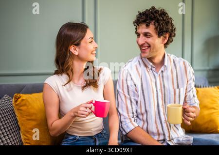 Portrait of happy adult couple sitting at sofa at home. They are looking at each other and smiling. Stock Photo