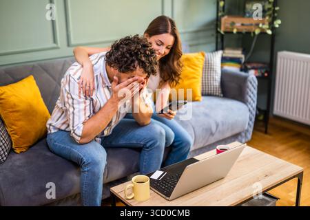 Woman is showing goods she wants to buy to her man. He is displeased. Online shopping. Stock Photo