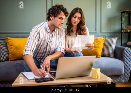 Couple discussing home finance while checking bills. They are checking financial documents and calculating family budget in living room. Stock Photo