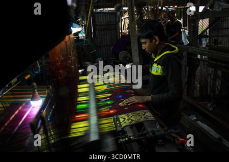Sirajganj, Bangladesh - 03 February 2021: View of a craftsman meticulously weaving vibrant threads into intricate patterns on a traditional loom in a bustling workshop. Stock Photo