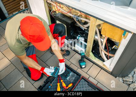 A spa technician kneels in front of an open refrigerator unit, inspecting components and organizing tools on the ground during a home repair in the la Stock Photo