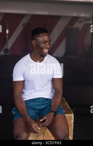 African American man sitting on wooden plyometric box at gym, wearing fitness tracker on wrist Stock Photo