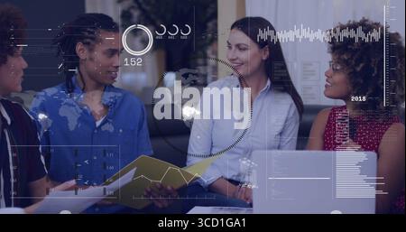 Discussing group of four coworkers using laptop and documents in office lounge, with data overlays Stock Photo