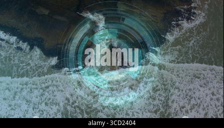 Displaying waves rolling along rocky shoreline in aerial view, with concentric circular HUD overlay Stock Photo