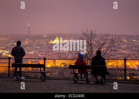 People overlooking night view of illuminated Prague on a misty evening sitting on a bench Stock Photo