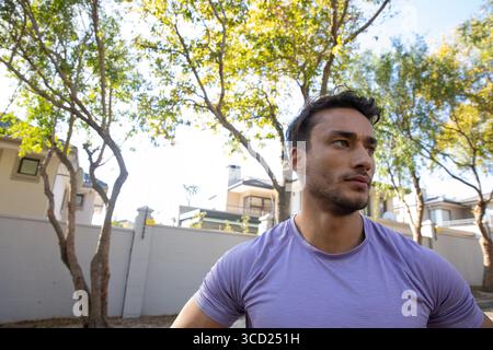 Man wearing purple athletic shirt standing by wall gazing right on suburban street, copy space Stock Photo