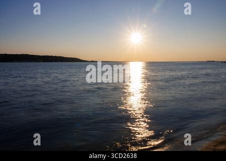 Sunset over ocean with golden light reflecting on water and shoreline Stock Photo
