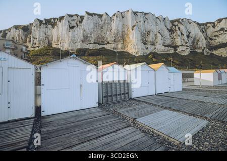 View of colorful beach huts line a wooden boardwalk against the backdrop of imposing chalk cliffs in the serene coastal town, Le Tréport, Normandy, Fr Stock Photo
