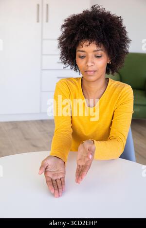 African American woman presenting palms above round table in modern living area with green sofa Stock Photo