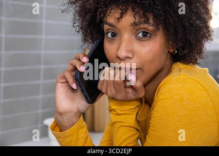 Woman leaning on kitchen countertop by backsplash while holding smartphone near wooden canisters Stock Photo