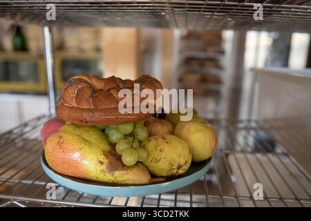 Plate with ripe pears green grapes apples and braided bread with poppy seeds placed on a metal shelf. Rustic food arrangement for kitchen bakery or ha Stock Photo