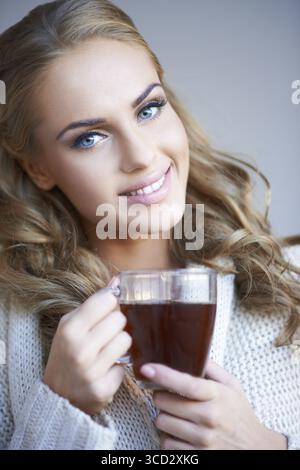 Smiling attractive woman with lovely long curly blond hair enjoying a mug of coffee as she looks at the camera with a friendly smile Stock Photo