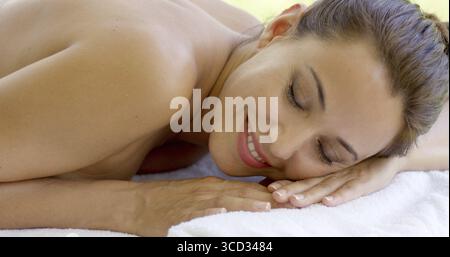 Adorable middle aged beautiful woman relaxing on spa table on outdoor patio closes her eyes and smiles to herself Stock Photo